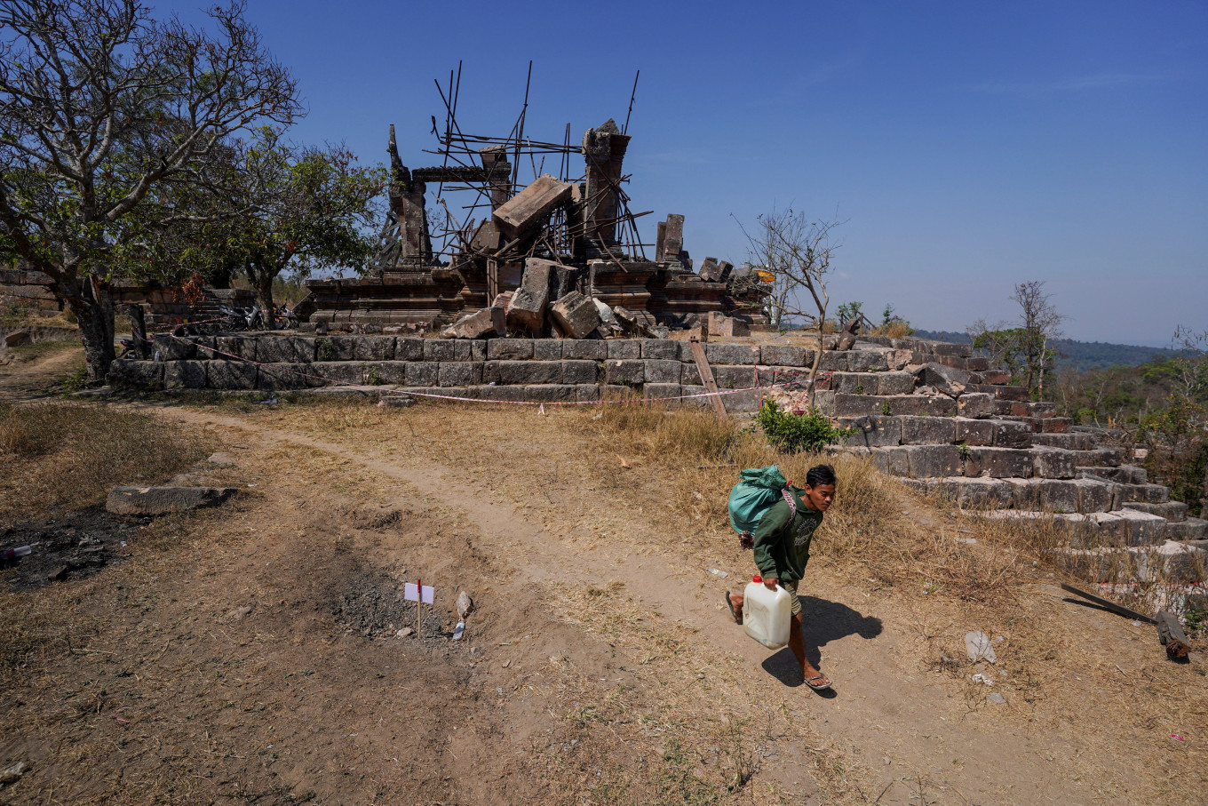 A person carries supplies on Feb. 12, 2026, as he walks past the damaged Preah Vihear temple, a UNESCO World Heritage site on the border between Thailand and Cambodia, following clashes between the two countries, in Preah Vihear province, Cambodia.