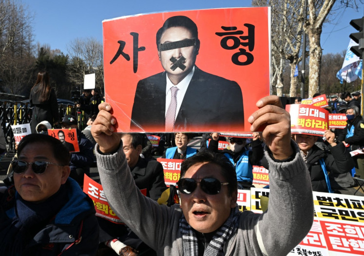 A protester holds a placard showing a photo of South Korea's impeached former president Yoon Suk Yeol reading &ldquo;A death sentence&ldquo; during a rally against Yoon near the Seoul Central District Court in Seoul on February 19, 2026.