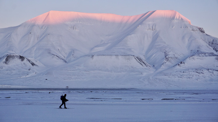 A man with a backpack and a rifle on his back makes his way on skis across a snowy landscape on Wednesday, Feb. 18, 2026, as the sunlight hits the summit of Hiorthfjellet in Longyearbyen, the administrative center of Norway&rsquo;s Svalbard archipelago.