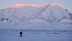 A man with a backpack and a rifle on his back makes his way on skis across a snowy landscape on Wednesday, Feb. 18, 2026, as the sunlight hits the summit of Hiorthfjellet in Longyearbyen, the administrative center of Norway&rsquo;s Svalbard archipelago.