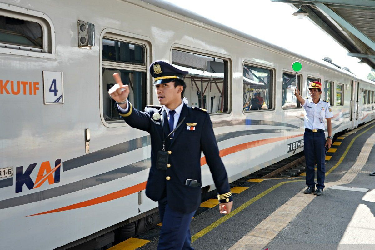 A train conductor (left) gives the sign to the train machinist (not pictured) to depart while the train dispatcher (right) lifts the green light baton at Medan train station. 