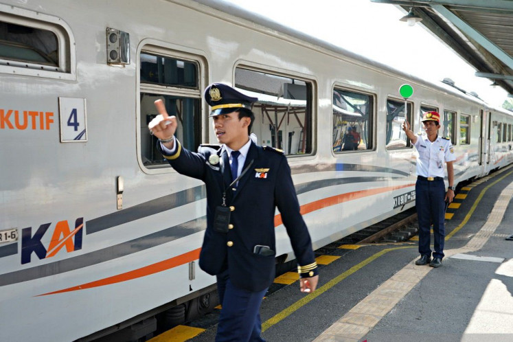 A train conductor (left) gives the sign to the train machinist (not pictured) to depart while the train dispatcher (right) lifts the green light baton at Medan train station. 