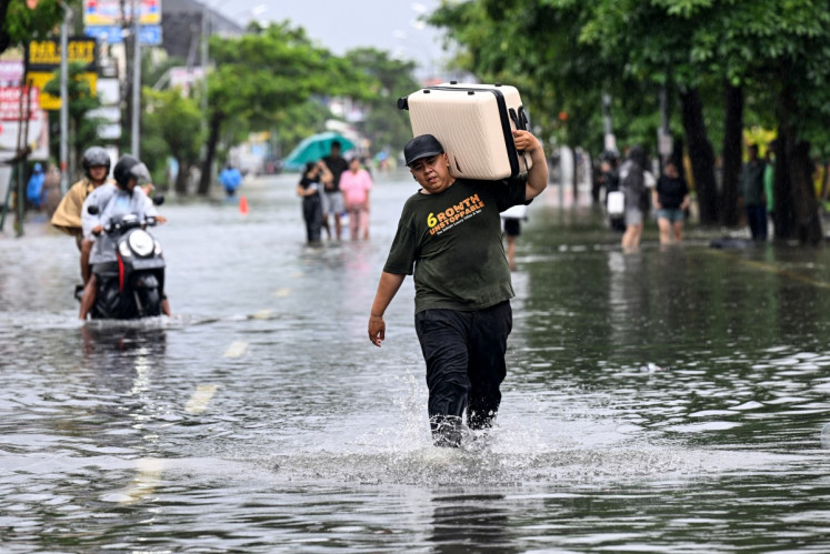 A hotel guest carries his suitcase as he wades through the water on an inundated street amid floods following heavy rain at Legian Kuta near Denpasar, Bali on February 24, 2026. 