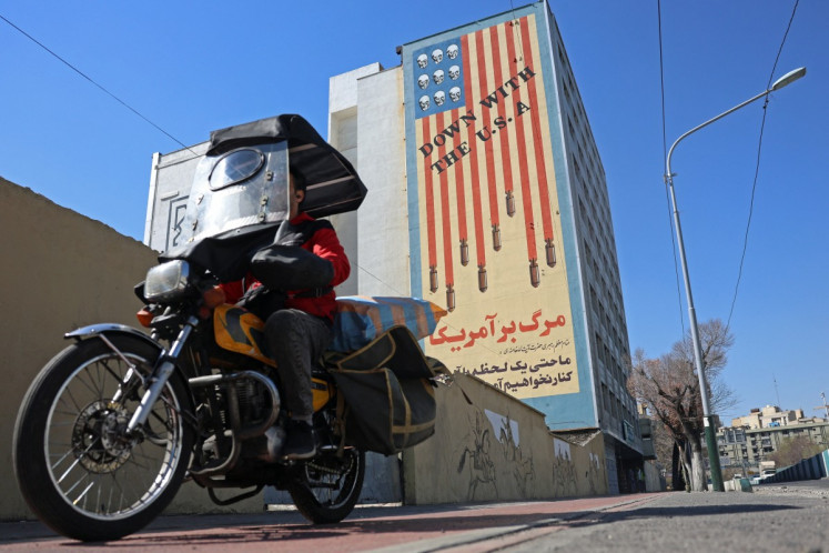 An Iranian man rides past an anti-United States mural on a building in Tehran, Iran on Feb. 26, 2026. A third round of indirect talks between the United States and Iran, mediated by Oman's foreign minister, opened in Geneva on Feb. 26 morning, a diplomatic source told AFP.