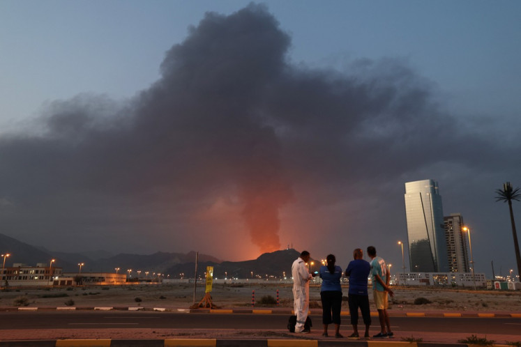 Foreign workers look at a tall plume of black smoke ascends following an explosion in the Fujairah industrial zone, UAE on March 3, 2026. 