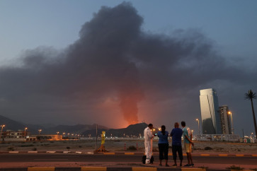 Foreign workers look at a tall plume of black smoke ascends following an explosion in the Fujairah industrial zone, UAE on March 3, 2026. 