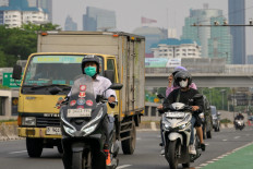 Motorists drive along a road while in the background buildings are shrouded by polluted air in Jakarta on Oct. 8, 2024.