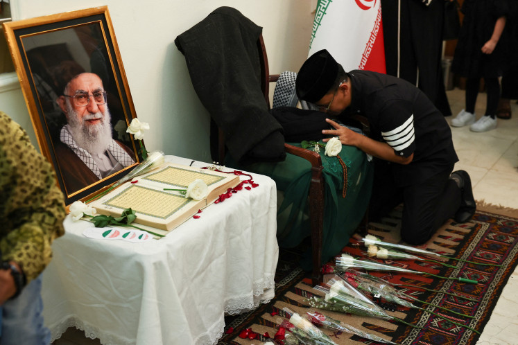 A man pays his respects to the late Iranian supreme leader Ayatollah Ali Khamenei (left, in framed picture) on March 5, 2026, during a prayer service at the Iranian ambassador's residence in Menteng, Central Jakarta.