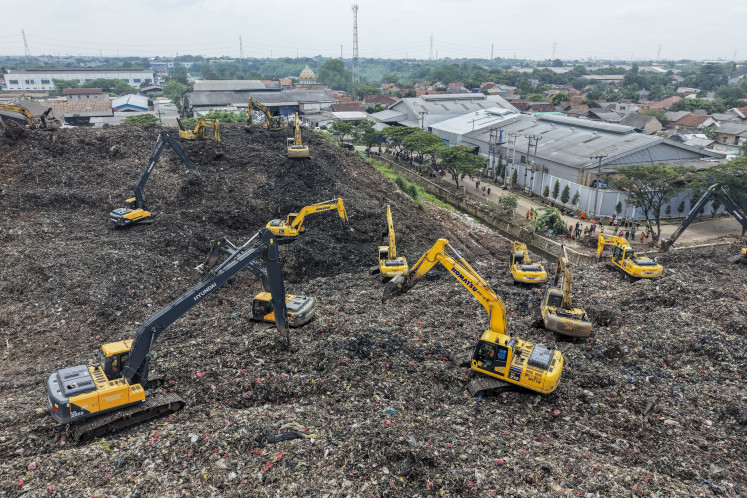 This aerial picture shows a rescue team using heavy machinery to search for people following a landslide at Bantargebang landfill in Bekasi, West Java, on March 9, 2026. A landslide on Indonesia's biggest landfill buried trucks and food stalls, killing four people, rescuers said on March 9 as they searched for at least five more reported missing.