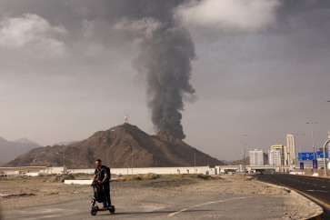 A person rides on a scooter as smoke rises in the Fujairah oil industry zone following a fire caused by debris after interception of a drone by air defenses, in Fujairah, United Arab Emirates, on March 3. 