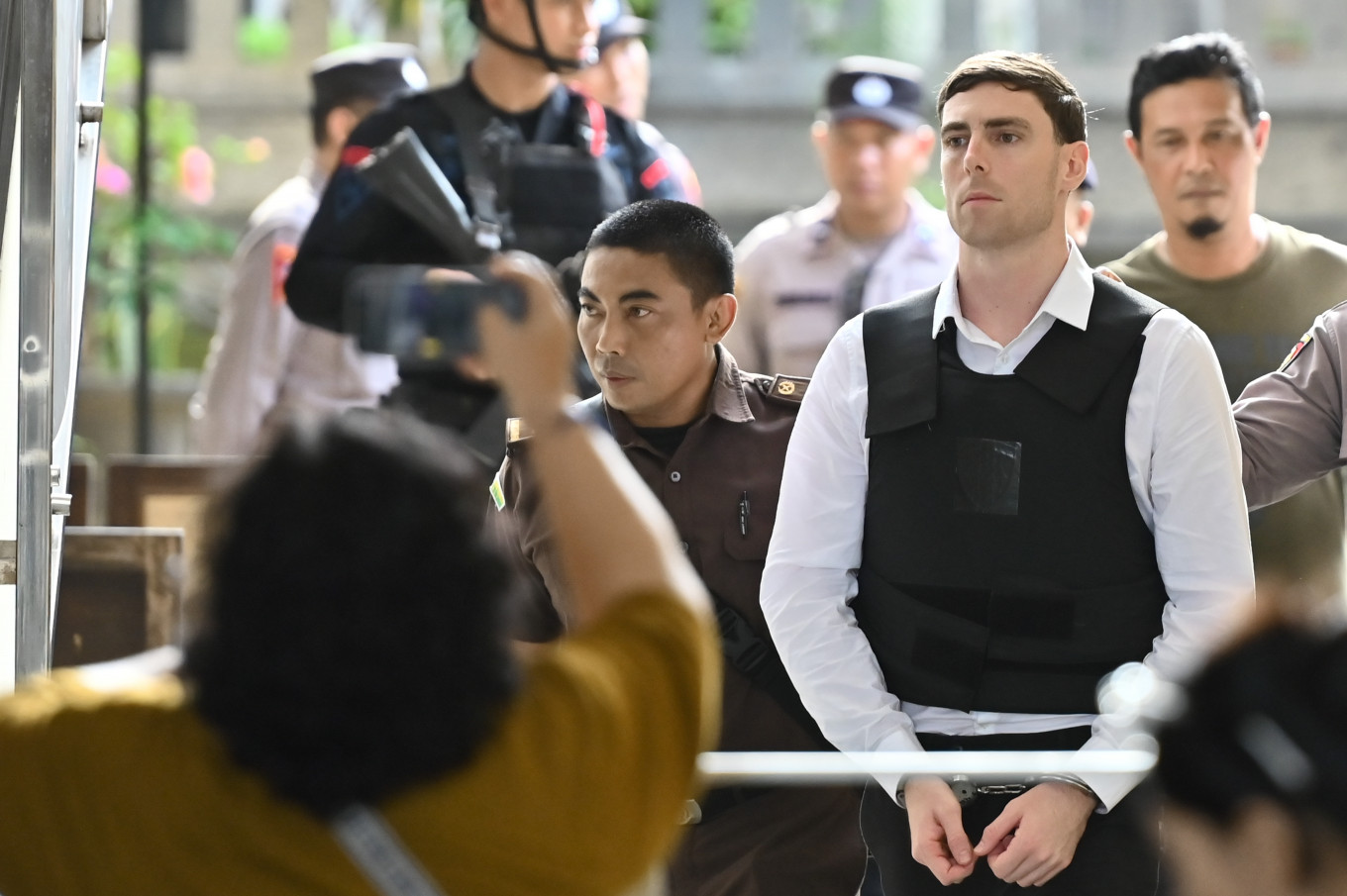 Australian national Darcy Francesco Jenson (second from right) is escorted by officers on March 9 after a verdict hearing at Denpasar District Court in Bali. He was sentenced to 12 years in prison for his role in the premeditated killing of fellow Australian Zivan Radmanovic and the wounding of Sanar Ghanim on June 14, 2025. 