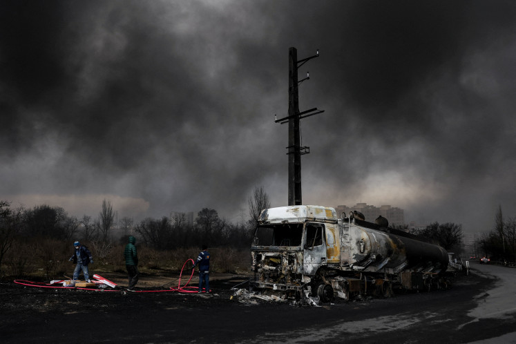 People stand near a destroyed vehicle as smoke rises after a reported strike on Shahran fuel tanks, amid the US-Israeli conflict with Iran, in Tehran, Iran on March 8, 2026. 
