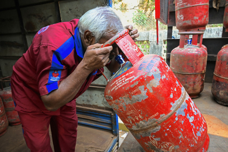 A deliveryman inspects a cylinder of liquefied petroleum gas (LPG) for leakage March 10, 2026, while unloading a batch of cylinders from a truck at a distribution point in Mumbai, India.