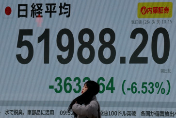 A Pedestrian stands in front of a stock quotation board showing the Nikkei share average outside a brokerage in Tokyo on March 9, 2026.