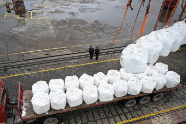Police officers watch as workers unload imported potash fertilizers from a cargo vessel at a bulk terminal in the port of Zhangjiagang, Jiangsu province, China, on March 18, 2026.