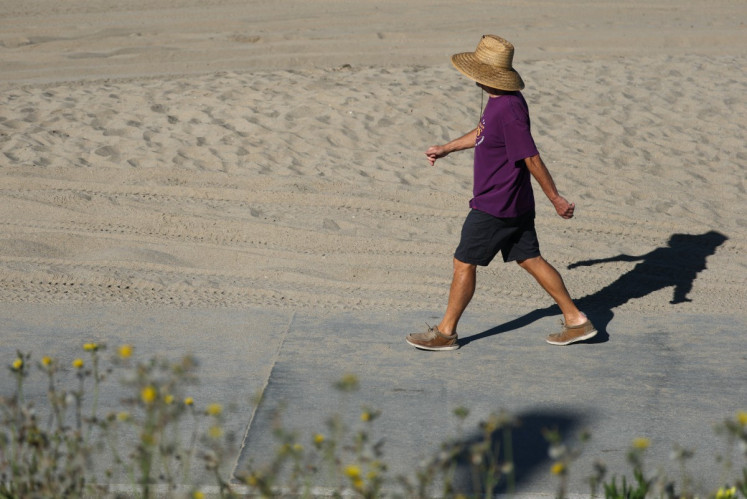 A person wears a hat for shade under the morning sun while walking along The Strand in Redondo Beach, California on March 20, 2026, during a heat wave. A record early heat wave striking the west of the United States on March 20 is a one-in-500-years type event and all but certainly the result of human-caused climate change, experts say.