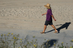 A person wears a hat for shade under the morning sun while walking along The Strand in Redondo Beach, California on March 20, 2026, during a heat wave. A record early heat wave striking the west of the United States on March 20 is a one-in-500-years type event and all but certainly the result of human-caused climate change, experts say.