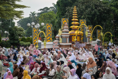 Muslim devotees listen to a preacher's sermon after the Idul Fitri prayers at city hall in Surabaya on March 21, 2026, in front of an installation on Balinese culture depicting the Nyepi holiday that is primarily observed on the island. A Swiss man faces hate speech charges in Bali over a social media post allegedly denigrating the Hindu celebration.