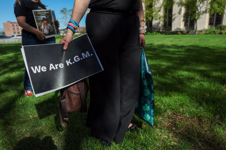A person holds a sign that reference a plaintiff, only identified by her initials, as people wait for a verdict in the social media trial tasked to determine whether social media giants deliberately designed their platforms to be addictive to children, in Los Angeles, on March 20, 2026.