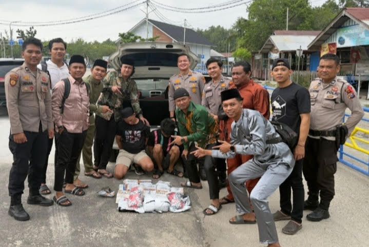 Bengkalis Police officers and detectives pose with two drugs 'mules' (center, squatting) and their contraband after arresting them at Air Putih ferry port in Air Putih village, Bengkalis district,  Riau, on March 21, 2026. 