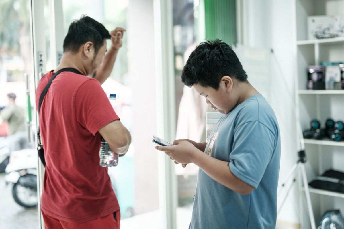 Bradley Rowen Liu, an 11-year-old boy learning Python, a programming language, watches a video on social media on his smartphone as he leaves the coding academy with his father Handri Liu in Jakarta on March 25, 2026. 