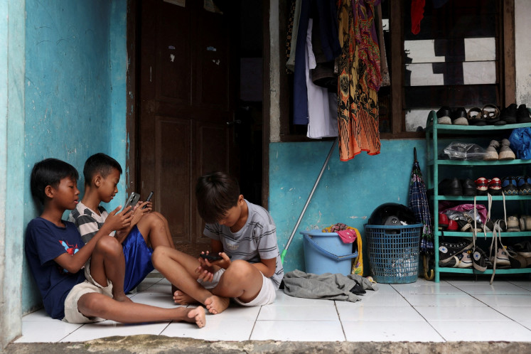 Children use their phones on March 28, 2026, in front of a house in Depok, West Java, the day the government implemented restrictions for under-16 users for &ldquo;high-risk&ldquo; social media and digital platforms, including Facebook, TikTok and Roblox.