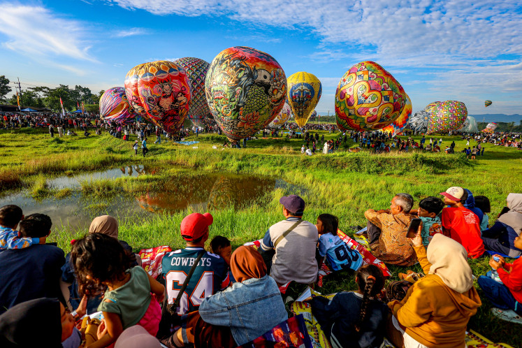 Residents watch hot air balloons take flight on March 29, 2026, at the motocross circuit in Ponorogo, East Java. The Ponorogo regency administration held the Reog Balon Carnival, involving 44 participating groups flying tethered balloons as part of efforts to promote tourism and culture in the area, as well as to regulate balloon use and prevent illegal launches that could disrupt air traffic.