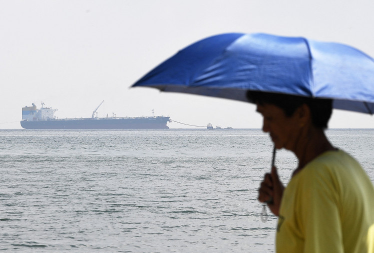 A man with an umbrella stands along the coast on March 26, 2026, against a backdrop of Sara Sky, a Sierra Leone-flagged tanker carrying Russian crude oil anchored at a jetty in Limay, Bataan province, the Philippines.