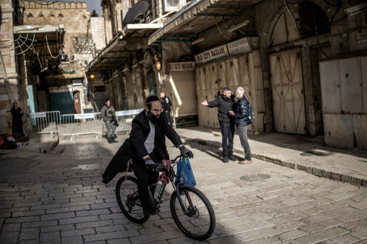 An Orthodox Jewish man rides his bicycle as an Israeli policeman (second right) argues with a Christian pilgrim who is refused entry to the Church of the Holy Sepulchre, where the Latin Patriarch of Jerusalem will celebrate Easter Sunday Mass, behind closed doors due to the ongoing war, in the old city of Jerusalem on April 5, 2026. 