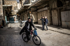 An Orthodox Jewish man rides his bicycle as an Israeli policeman (second right) argues with a Christian pilgrim who is refused entry to the Church of the Holy Sepulchre, where the Latin Patriarch of Jerusalem will celebrate Easter Sunday Mass, behind closed doors due to the ongoing war, in the old city of Jerusalem on April 5, 2026. 