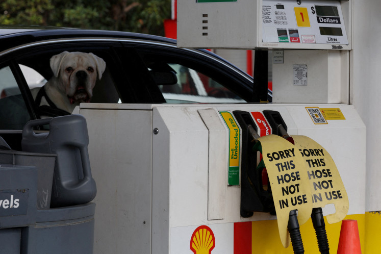 A dog looks out of a car window next to signs on empty fuel dispensers at a Shell gasoline station that ran out of fuel, in Sydney, Australia, on March 30, 2026.