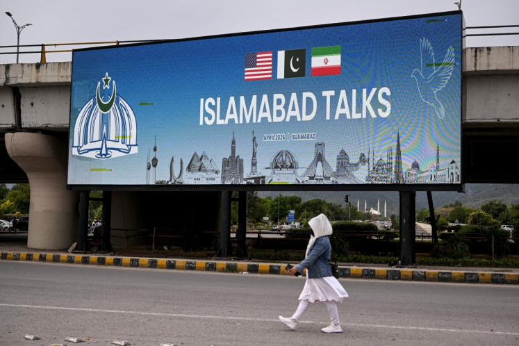 A woman walks past a digital screen displaying news of United States-Iran peace talks along a road in Islamabad, Pakistan on April 10, 2026. A cloud of uncertainty hung April 10 over the scheduled start of talks in Pakistan between the United States and Iran, with no announcement yet on the arrival of negotiators and both sides accusing the other of failing to properly implement a fragile ceasefire.
