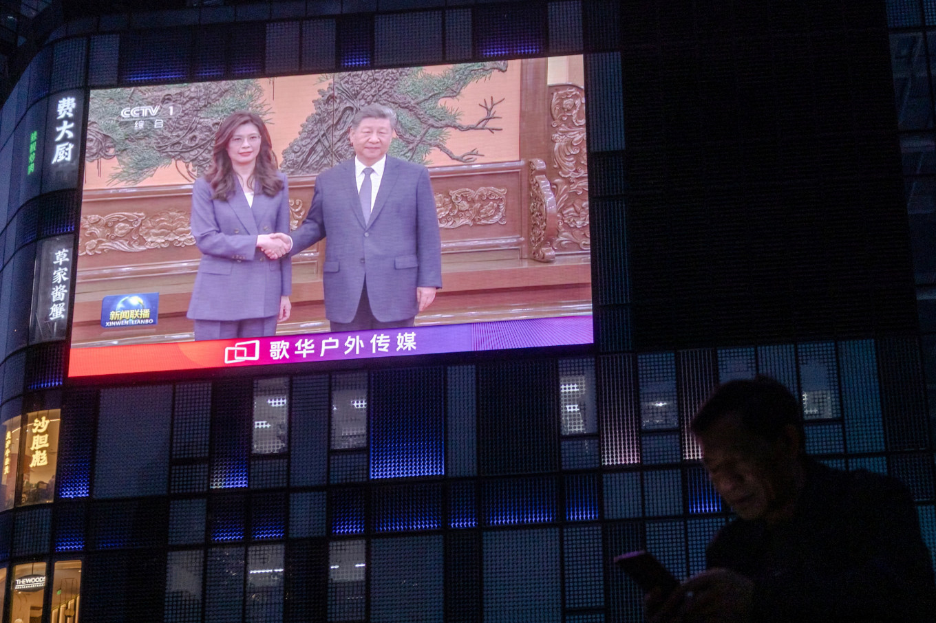 A man uses his smartphone as a giant screen broadcasts news showing Chinese President Xi Jinping shaking hands with Cheng Li-wun, chairperson of the Kuomintang (KMT), Taiwan's largest opposition party at the Great Hall of the People in Beijing, China, April 10, 2026.