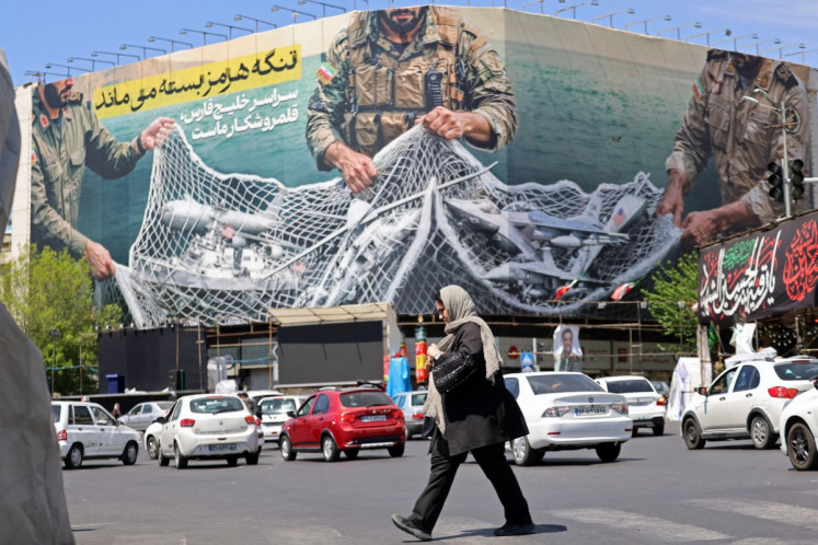 A woman walks past a giant billboard reading 'The Strait of Hormuz remains closed' at the Revolution Square in Tehran on April 12, 2026.