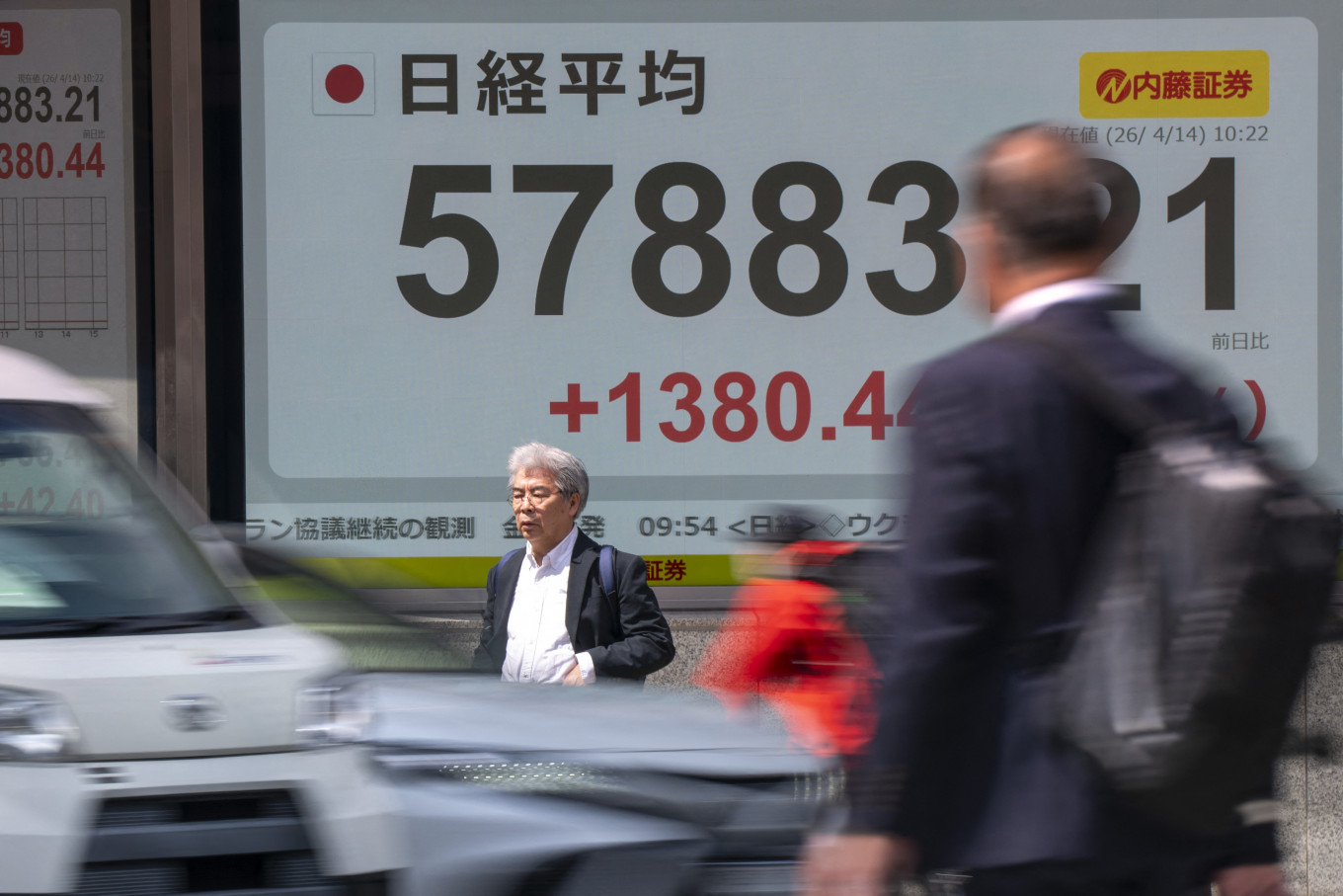 People walk past an electronic quotation board displaying the Nikkei Stock Average on the Tokyo Stock Exchange along a street in Tokyo on April 14, 2026.