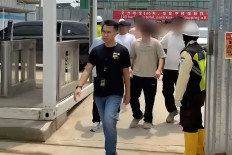 An officer from Bekasi Immigration Office (left) leads foreign workers (blurred) who were netted during Operation Wira Waspada at a construction site in Greenland International Industry Center in Deltamas, Central Cikarang, Bekasi regency, West Java, on April 8, 2026.