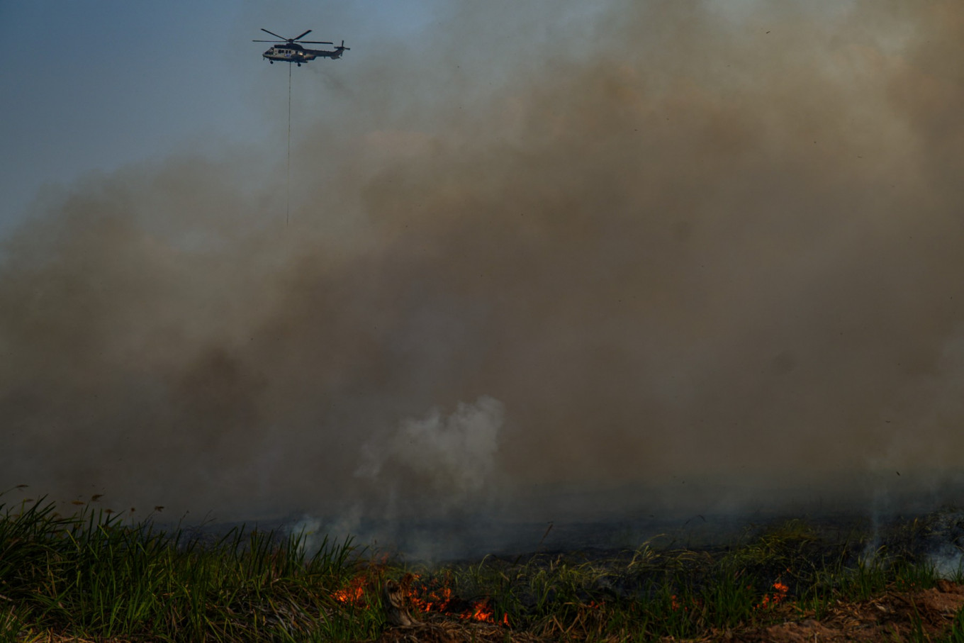 A helicopter from the National Disaster Management Agency drops waterbombs to combat a wildfire in the peatlands of Ogan Ilir, South Sumatra, on September 26, 2025. 