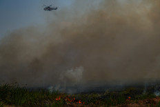 A helicopter from the National Disaster Management Agency drops waterbombs to combat a wildfire in the peatlands of Ogan Ilir, South Sumatra, on September 26, 2025. 