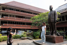 A law graduate poses on April 16, 2026, for a photo with the statue of noted legal scholar Djokosoetono, the founding dean of the University of Indonesia&rsquo;s (UI) Faculty of Law in the faculty&rsquo;s campus in Depok, West Java, after receiving her graduation certificate. UI has suspended 16 law students after a sexually explicit group chat about their female peers went viral, sparking a debate about gender violence.