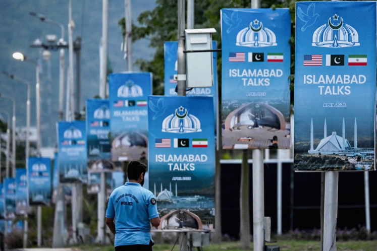 A police personnel walks past posters highlighting Pakistan's mediation of Iran-US peace talks, at the Red Zone area in Islamabad on April 18, 2026.