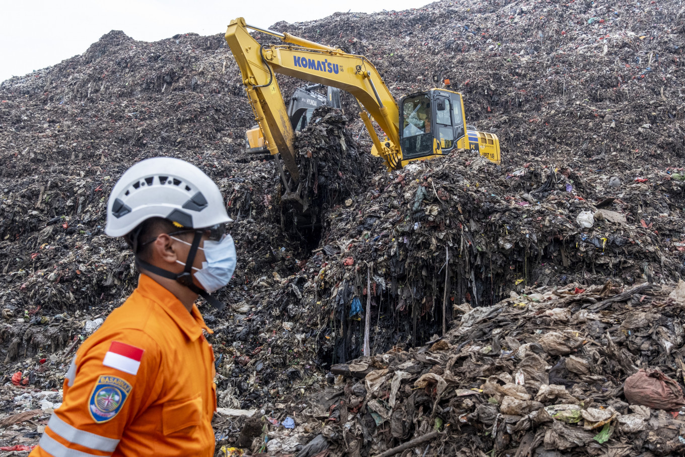A rescue worker monitors an operation using heavy machinery to search for missing people on March 9, 2026, after a landslide buried trucks, food stalls and at least 13 people at the Bantar Gebang landfill in Bekasi, West Java.