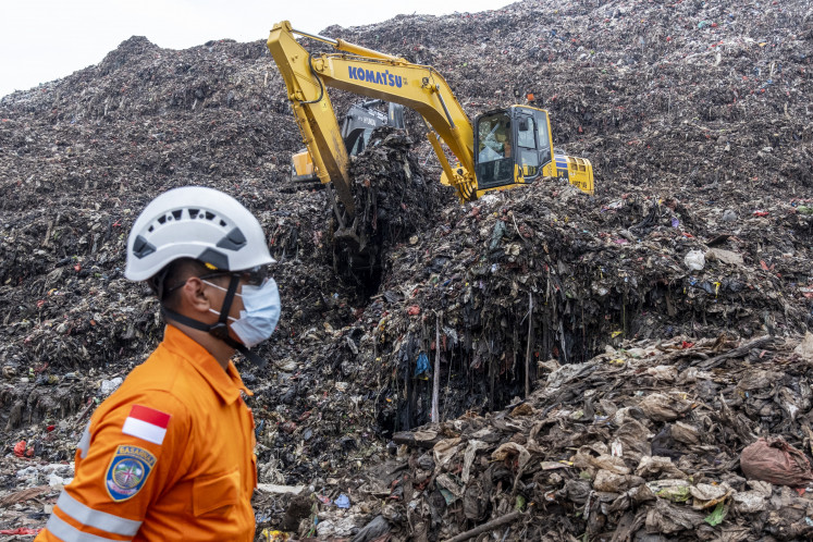 A rescue worker monitors an operation using heavy machinery to search for missing people on March 9, 2026, after a landslide buried trucks, food stalls and at least 13 people at the Bantar Gebang landfill in Bekasi, West Java.