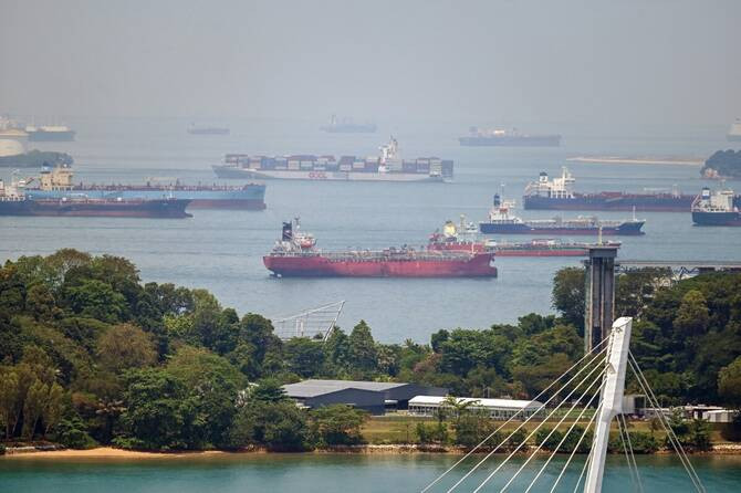 A container ship sails past oil tankers anchored in the Singapore Strait, a key gateway to the Strait of Malacca, on April 14, 2026. 