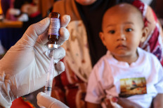 A child looks as a medical worker prepares a dose of measles vaccine in Makassar, South Sulawesi on April 14, 2026. The South Sulawesi Health Agency launches a measles immunization drive following 169 cases of diseases found across the province.