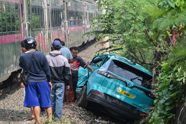 A train passes beside a damaged Green SM electric taxi following a collision between a commuter train and the Argo Bromo Anggrek train at East Bekasi Station in Bekasi, West Java, on April 28, 2026.
