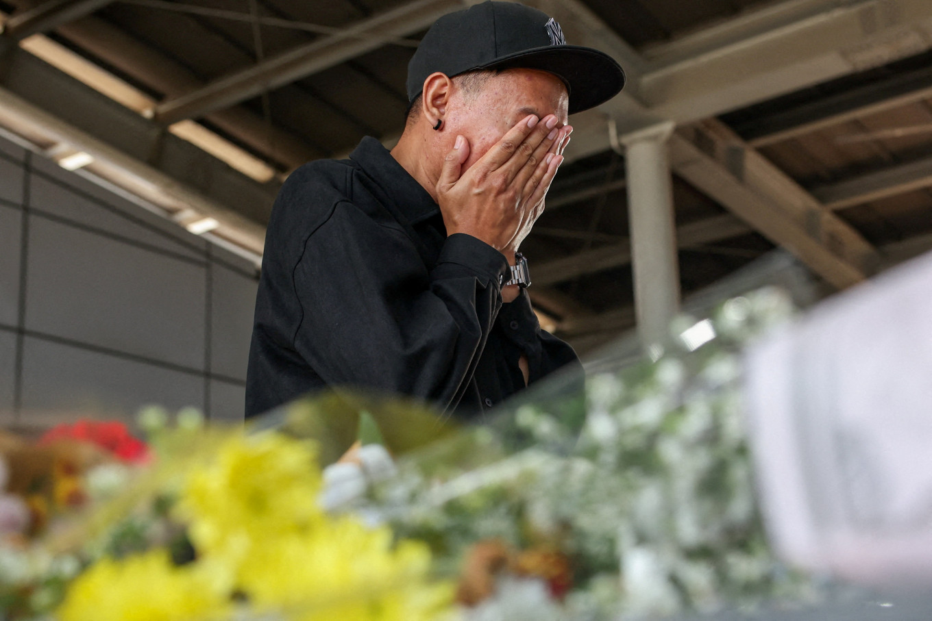 A passenger reacts near bouquets of flowers left in tribute for victims of the deadly collision between a commuter train and an intercity train, at Bekasi Timur Station in Bekasi, West Java, April 30, 2026. 