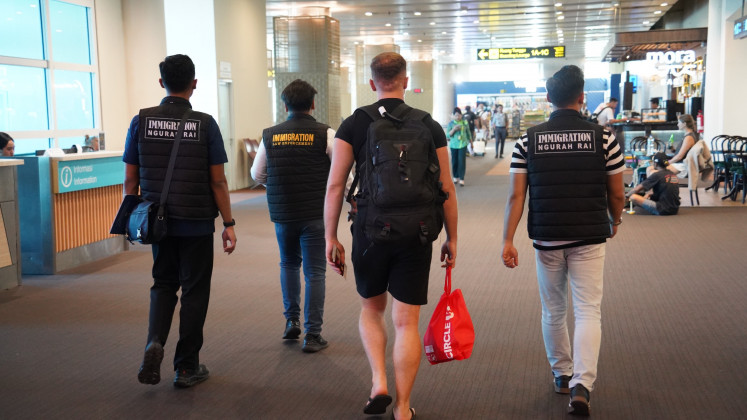 Officers from Ngurah Rai Immigration Office escort Italian tourist IG (second right) on Tuesday as he was deported to Doha from I Gusti Ngurah Rai International Airport in Badung regency, Bali. The tourist was deported because of a physical altercation with a traffic police officer in Denpasar after IG refused to be ticketed for not wearing a helmet while riding a motorcycle on April 22, 2026. 