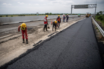 Workers from PT Waskita Sriwijaya, a subsidiary of state-owned construction firm Waskita Karya, use rakes on April 3, 2023, to spread asphalt along a section of the Trans-Sumatra Toll Road in Ogan Komering Ilir regency, South Sumatra. 