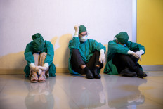Health workers sit against a wall in this undated stock illustration of overworked doctors.