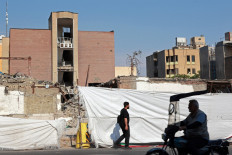 A motorist rides a motorcycle while a man walks past the Alameh Tabatabaei high school, which was destroyed by a US-Isareli airstrike during the war, in Tehran on May 3, 2026. 